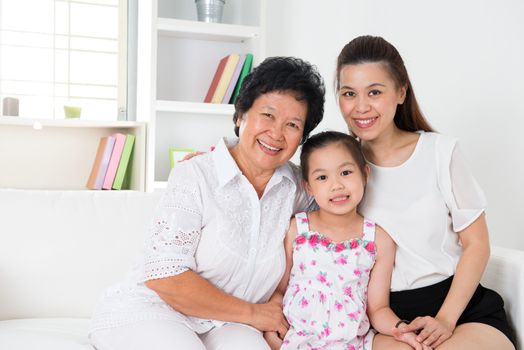 Family generations. Happy Asian family at home, grandparent, parent and grandchild sitting on sofa smiling looking at camera.