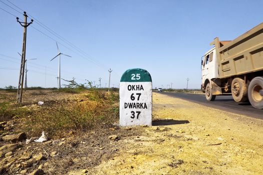 Horizontal, color landscape with Dwarka milestone and direction sign in the state highway 25 of Gujarat India caught with a truck passing in this barren wilderness region of India