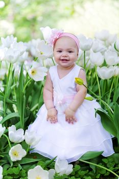 little girl in an elegant dress to stand near blossoming tulips