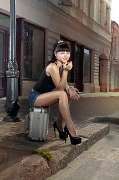 woman sits on suitcase near road in the small ancient city