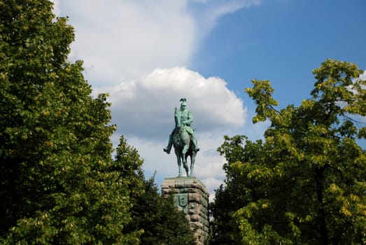 Monument to Kaiser Wilhelm at the Hohenzollern Bridge framed by trees in Cologne, Germany