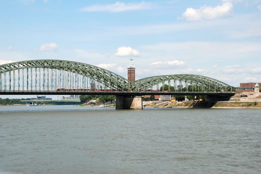 A train crosses the Hohenzollernbruecke (Hohenzollern Bridge) over the Rhine in Cologne, Germany. Beyond stands the Messeturm and to the right a monument to Kaiser Wilhelm.