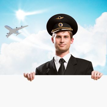 pilot in the form of holding an empty billboard on the background of sky and flying plane, place for text