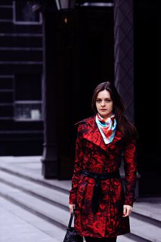 Beautiful business woman in a red cloak against expensive office building