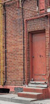 A distressed red door with external electrical components in an urban setting