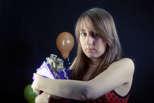 sad girl with a gift box on a dark background with balloons