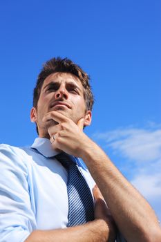Young business man looking up against a blue sky