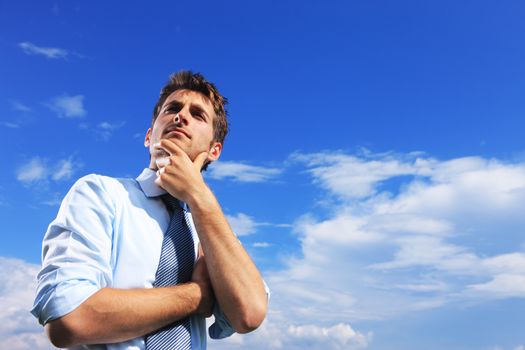 Young business man thinking against blue sky