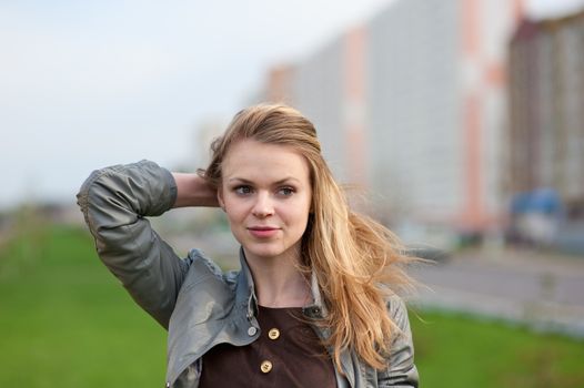 The young pleasant smiling girl with long hair costs against the building under construction