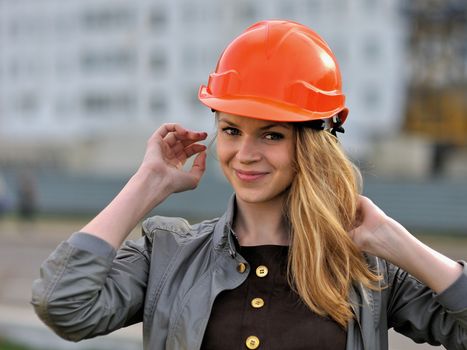 The young pleasant smiling girl with long hair costs against the building under construction