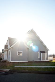 Modern custom built house newly constructed in a residential neighborhood with strong lens flare.  Gas fireplace bump out visible on the side.