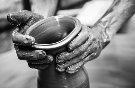 Hands of a man creating pottery on wheel, monochrome vintage view