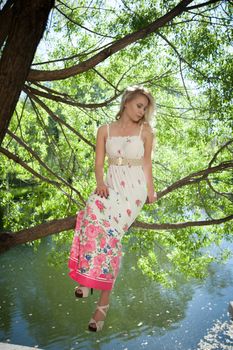 beautiful blonde sitting in a tree above the water in the park