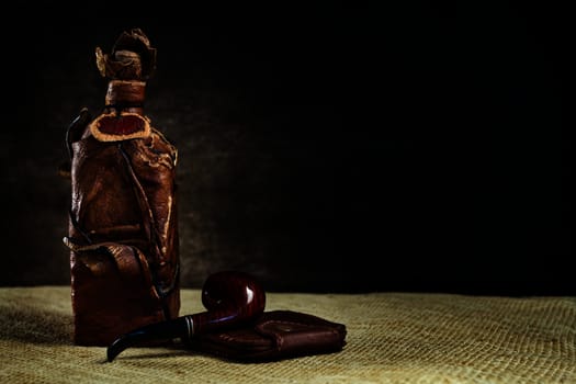 Brown leather vintage bottle with a pipe and a purse on a dark background