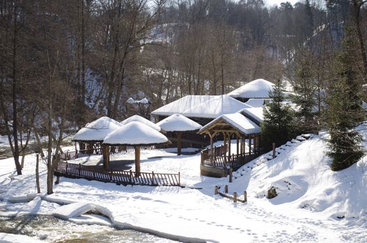 frozen river bay water and small wooden houses on bank with straw roof covered with snow.