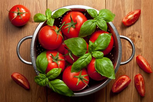 Tomatoes with basil in colander on wooden table background. Food composition. Top view