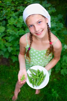 Beautiful girl holding plate of green Peas in garden