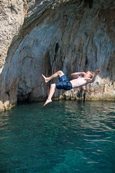 Deep water soloing, young male rock climber jumping from a cliff