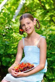 Beautiful little smiling girl eating cherries in garden