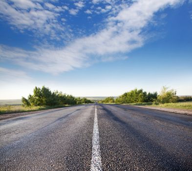 asphalt road through the green field and clouds on blue sky in summer day