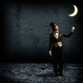magician in top hat and tie, holding a glowing moon on a string