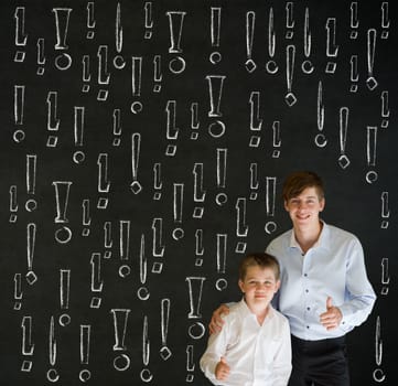 Thumbs up boy dressed up as business man with teacher man and chalk exclamation marks on blackboard background