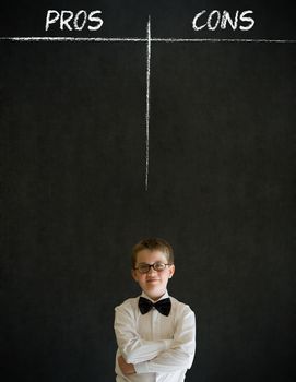 Thinking boy dressed up as business man with chalk pros and cons decision list on blackboard background