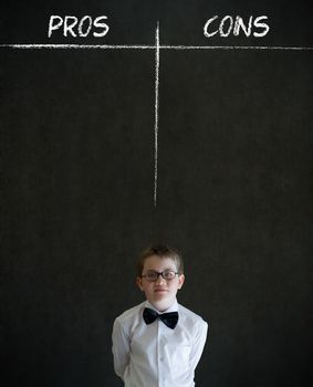 Thinking boy dressed up as business man with chalk pros and cons decision list on blackboard background