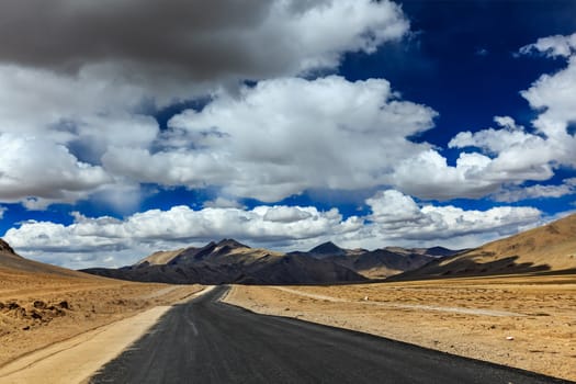 Travel forward concept background - road on plains in Himalayas with mountains and dramatic clouds. Manali-Leh road, Ladakh, Jammu and Kashmir, India