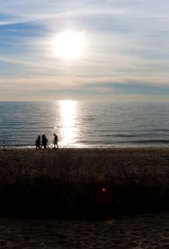 Silhouette of a family walking along the New England shoreline with lens flare.