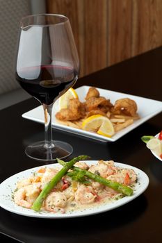 A delicious shrimp scampi pasta dish with red wine and friend shrimp appetizer in the background.