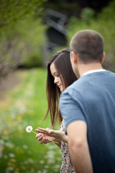 Woman with her boyfriend holding a dandelion outdoors.