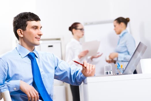 Portrait of a businessman in a blue shirt in the background of colleagues discussing