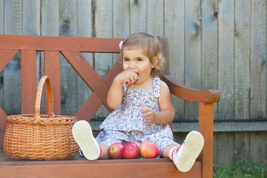 Little girl in a summer dress sits on a wooden shop with apples