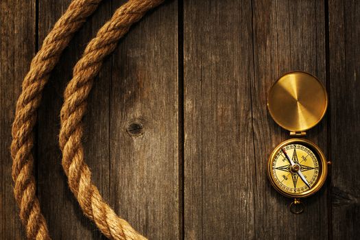 Antique brass compass and rope over wooden background