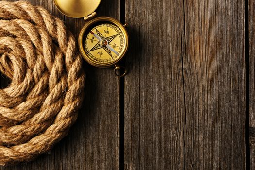 Antique brass compass and rope over wooden background