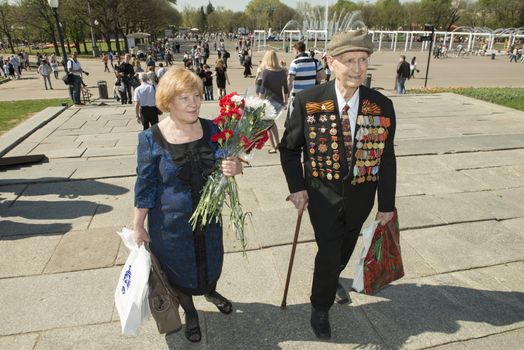  Moscow, Russia - May 9, 2013: Old man veteran of WWII in uniform decorated with numerous orders and medals and his douther bearing bunch of flowers during festivities devoted to 68th anniversary of Victory Day.