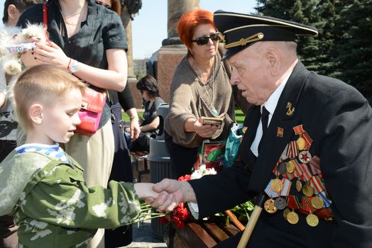 Moscow, Russia - May 9, 2013: Old man veteran of WWII in uniform decorated with numerous orders and medals bearing bunch of flowers accept  a congratulations from a young boy during festivities devoted to 68th anniversary of Victory Day.