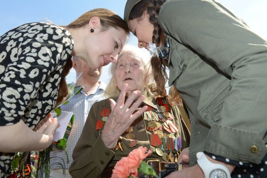 Moscow, Russia - May 9, 2013: Old woman veteran of WWII in uniform decorated with numerous orders and medals bearing bunch of flowers tells the story of the war the two girls during festivities devoted to 68th anniversary of Victory Day.