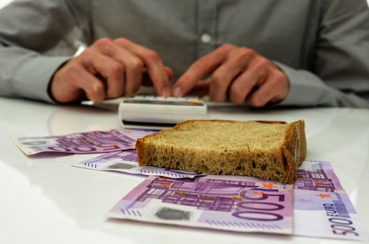 Slice of bread on Euro banknotes with male hand calculating food expenses in background. 