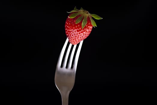 fresh strawberry on fork isolated on black background
