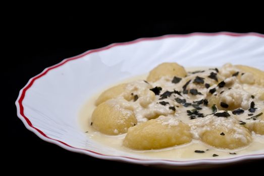 italian gnocchi with four cheese sauce isolated on black background