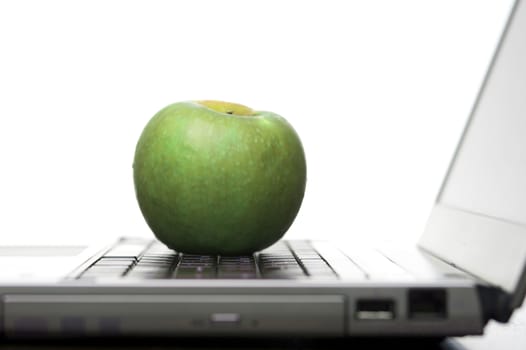 Green apple resting on the keyboard of an open laptop computer in an education and healthy eating concept, low angle against a white background