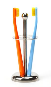 Two color toothbrushes in a metal holder on white
