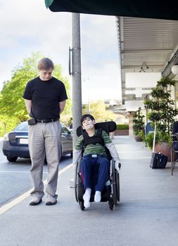 Father walking next to disabled six year old son in wheelchair through town. Son has cerebral palsy.
