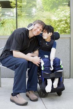 Disabled six year old boy in wheelchair hugging father while waiting at hospital