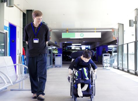 Father walking with disabled son in wheelchair as he wheels himself into the hospital entrance