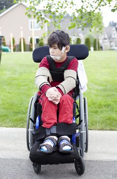 Disabled biracial six year old boy sitting in wheelchair on sidewalk