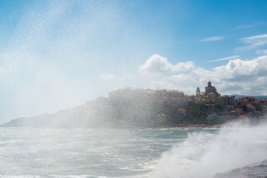 Beautiful old town of Imperia in Liguria at the Italian Riviera seen through spray during heavy waves on the pier