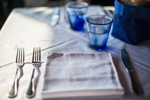 Table set for cozy dinner with blue glasses, bread basket and cutlery